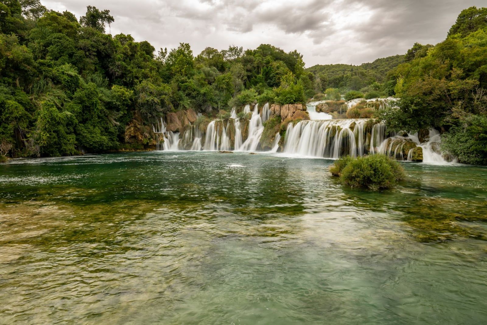 Cascades de travertin de Skradinski Buk se déversant dans un bassin de rivière vert et calme entouré de forêt dans le parc national de Krka.