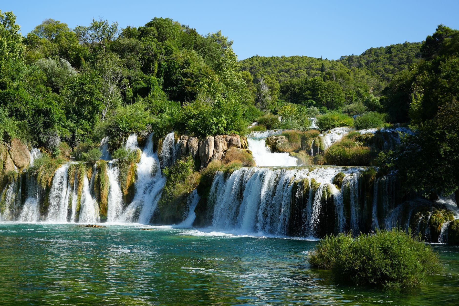 Tiered waterfalls cascade into a turquoise pool framed by lush green hills in Krka National Park.