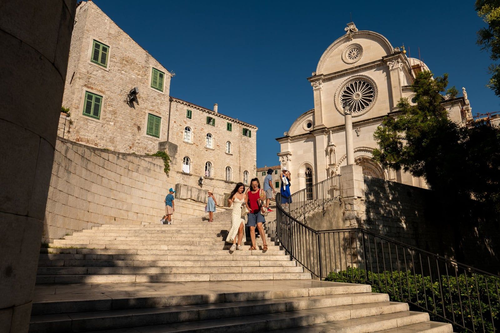 Visitantes bajando por la escalera de piedra junto a la catedral de Santiago en Šibenik en un día soleado.