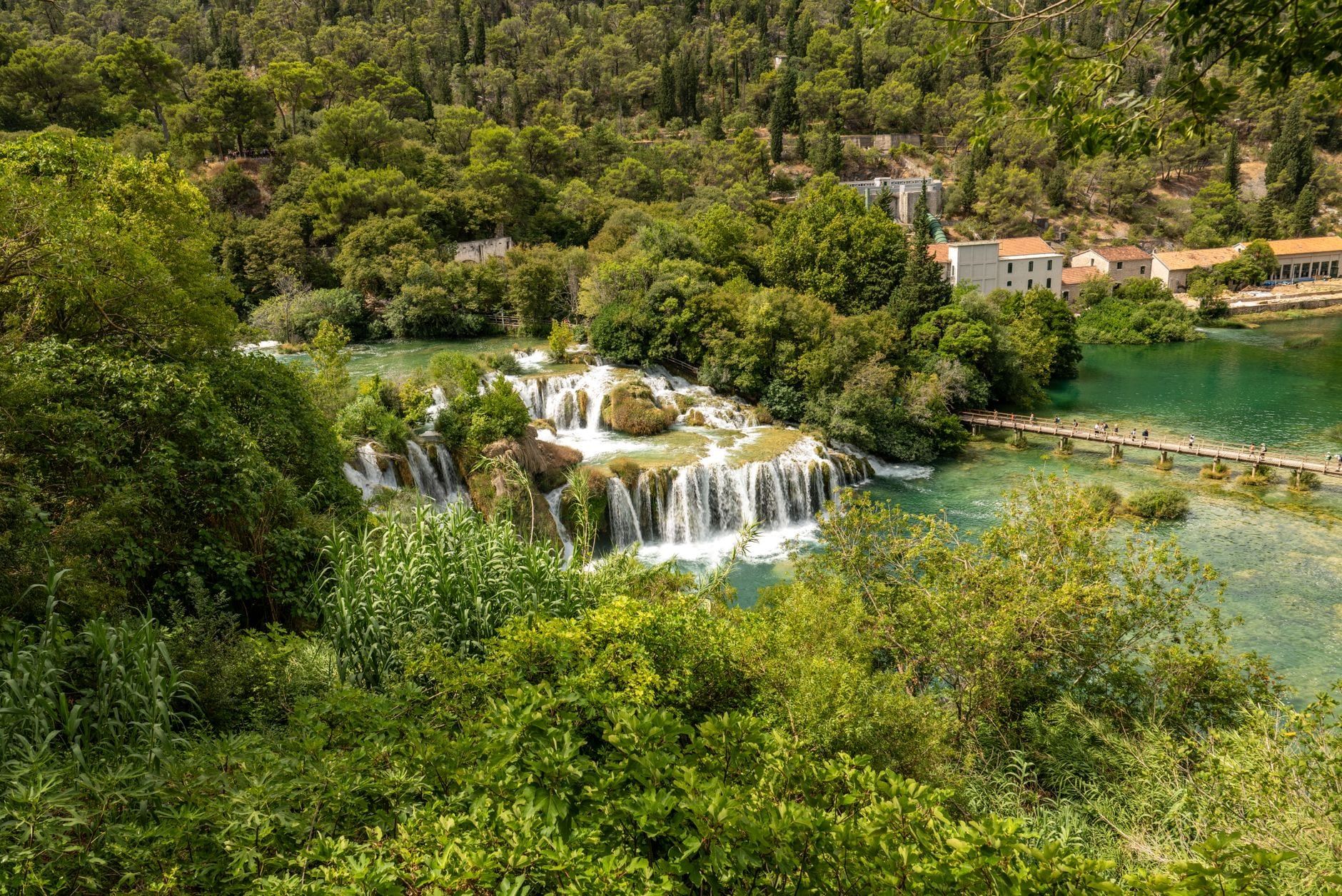 Eine erhöhte Aussicht auf die Wasserfälle des Skradinski Buk, die durch üppigen Wald in einen türkisfarbenen Fluss im Krka-Nationalpark hinabstürzen.